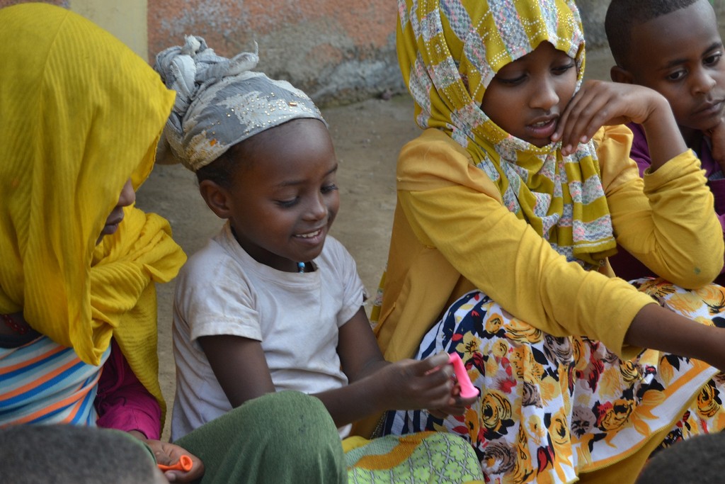 Drei Kinder sitzen mit schönen Kleidern am Straßenrand und spielen. Die Aufnahme ist in einem Dorf in der Nähe der Bio Fairtrade Kaffee Kooperative in Äthiopien, die Wiege des Kaffees, entstanden.