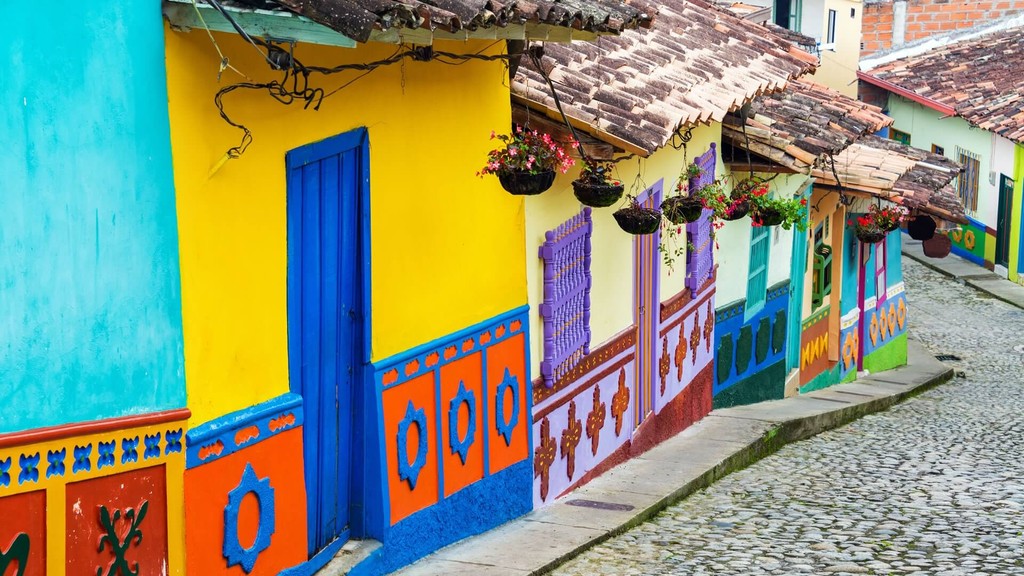 Sie sehen eine bunte Häuserfront in einem Dorf in Kolumbien in der Nähe der Bio Fairtrade Kaffee und Kakao Kooperative. Die ebenen Häuser haben einfache Dächer und sind sehr schön farbenfroh bemalt. 