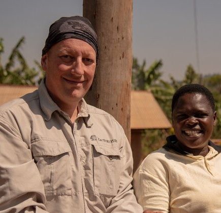 Sie sehen ein Bild von Gerhard dem Chef von Life Earth Reisen. Er hat Kaffeebohnen in seinen Händen und neben ihm steht eine Kaffeebäuerin aus Uganda von einer Bio Fairtrade Kaffee Farm. 