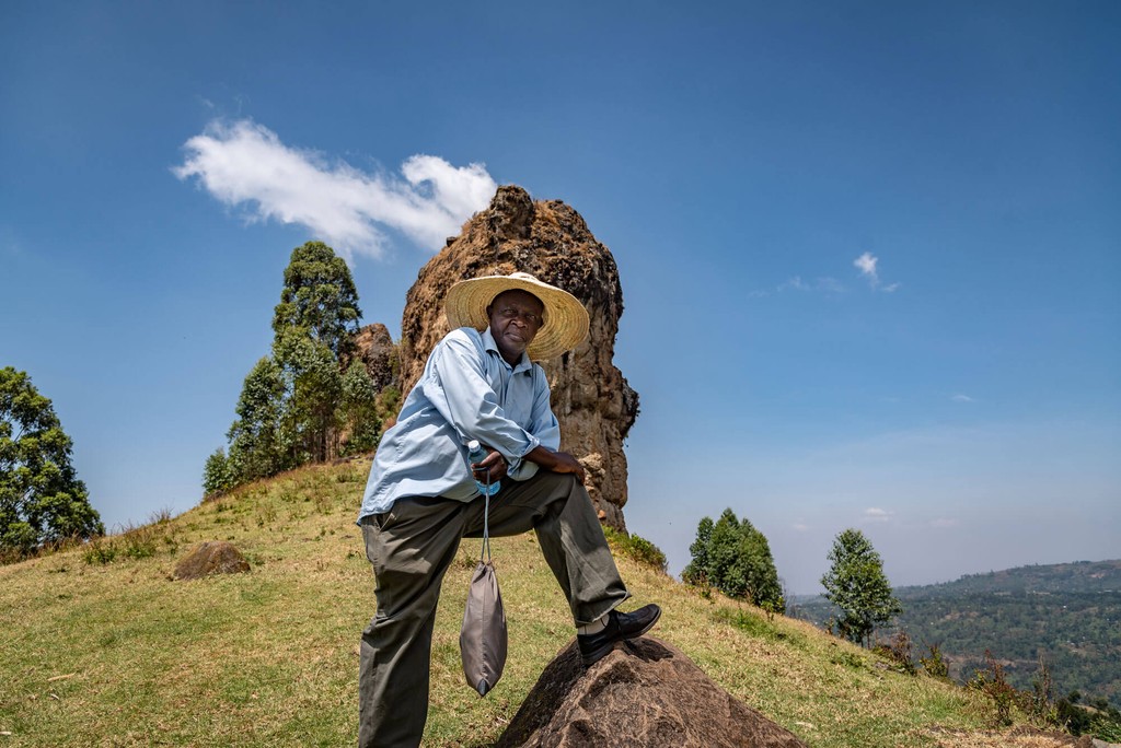 Sie sehen Nimrod den Chef der Kooperative am Berg Mount Elgon stehend. Das Foto ist bei der Kaffee Reise 2019 beim Besuch der Bio Fairtrade Kaffee und der Betriebsbesichtigung der Bio Fairtrade Kaffee Kooperative Bauern in Uganda entstanden. Wir führen durch alle Schritte der Kaffee Herstellung. Nimrod trägt seinen typischen Kaffeehut.