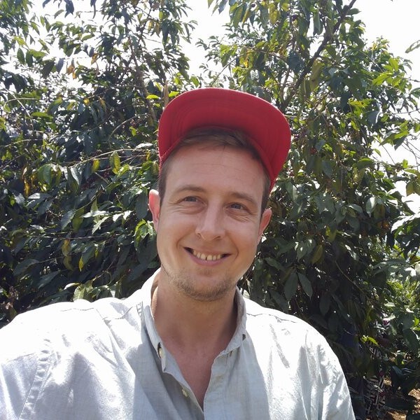 Sie sehen Thomas wie er vor dem Kaffeesträuchern steht und lacht. Das Bild ist im Kaffeegarten der Bio und Fairtrade Bauern in Sri Lanka entstanden,