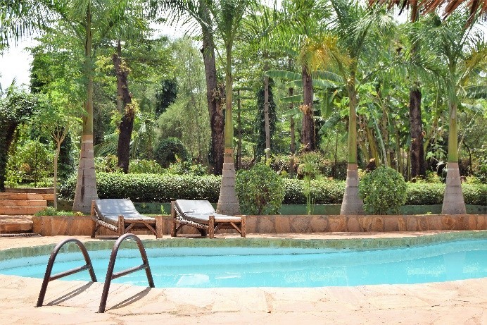 Sie sehen ein Foto des Pools der sehr schönen Chanya Lodge in Moshi. Hier werden wir zwei Nächte verbringen. Im Hintergrund sehen Sie die Palmen und die schöne gepflegte Hotelanlage.