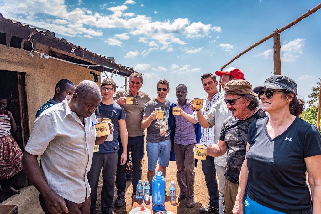 Ein Foto von der Kaffee Reise nach Uganda. Sie sehen die Mitglieder der Fairtrade Bio Kaffee Kooperative, Reisebegleiter Thomas Angerer und Teilnehmer der Kaffee Reise. Alle trinken Kaffee der lokalen Fairtade Bio Kaffee Bauern Familie.